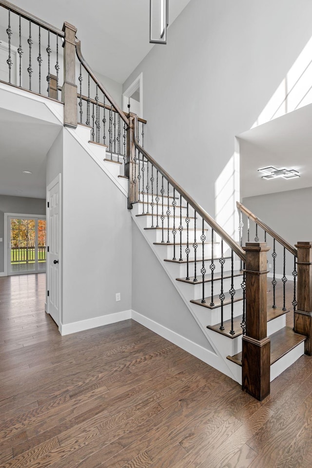 stairs with a towering ceiling, baseboards, and wood finished floors