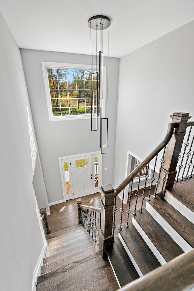 staircase featuring baseboards, a high ceiling, and wood finished floors