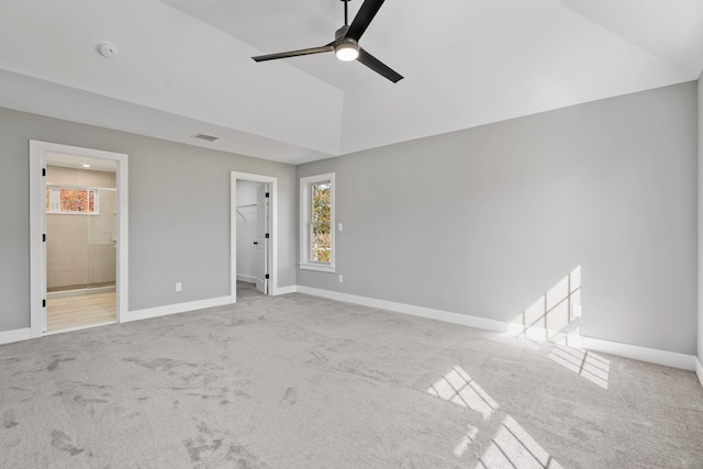 unfurnished bedroom featuring carpet, a walk in closet, lofted ceiling, ensuite bath, and baseboards