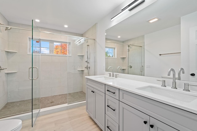 bathroom with a stall shower, wood finished floors, a sink, and double vanity