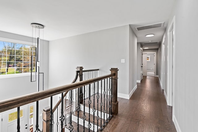 corridor with dark wood-style floors, baseboards, visible vents, and an upstairs landing