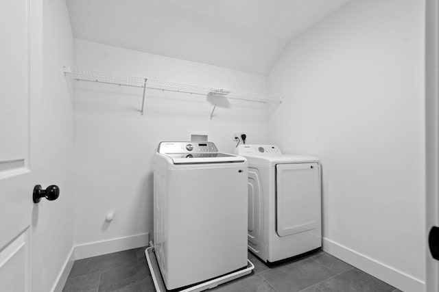 clothes washing area with laundry area, separate washer and dryer, dark tile patterned flooring, and baseboards