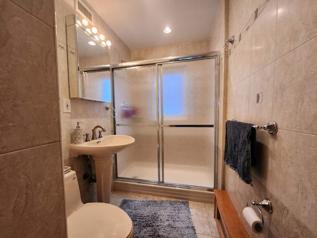 bathroom featuring toilet, tile walls, and a shower with door