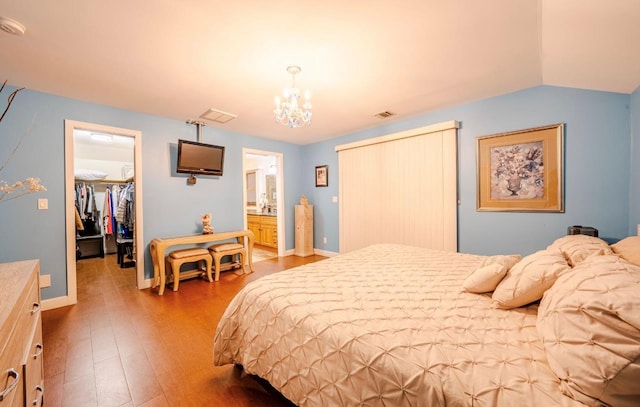 bedroom featuring lofted ceiling, hardwood / wood-style floors, connected bathroom, a walk in closet, and a closet