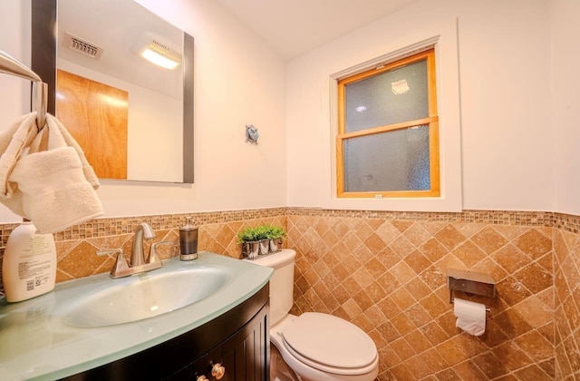 bathroom with toilet, tile walls, and vanity