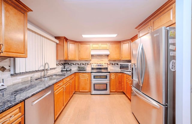 kitchen with appliances with stainless steel finishes, dark stone countertops, decorative backsplash, sink, and light hardwood / wood-style flooring