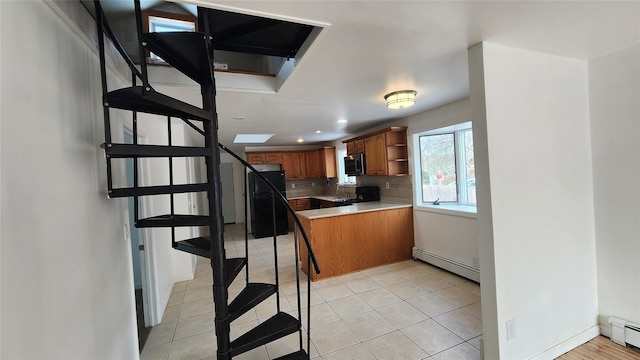 kitchen with light tile patterned floors, black fridge, kitchen peninsula, baseboard heating, and decorative backsplash