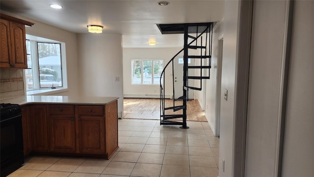 kitchen featuring light tile patterned floors, stove, a baseboard radiator, and kitchen peninsula