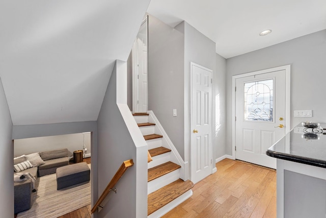 foyer entrance featuring baseboards, light wood finished floors, and stairs