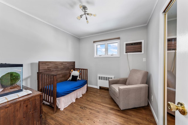 bedroom with radiator heating unit, ornamental molding, an AC wall unit, wood finished floors, and baseboards