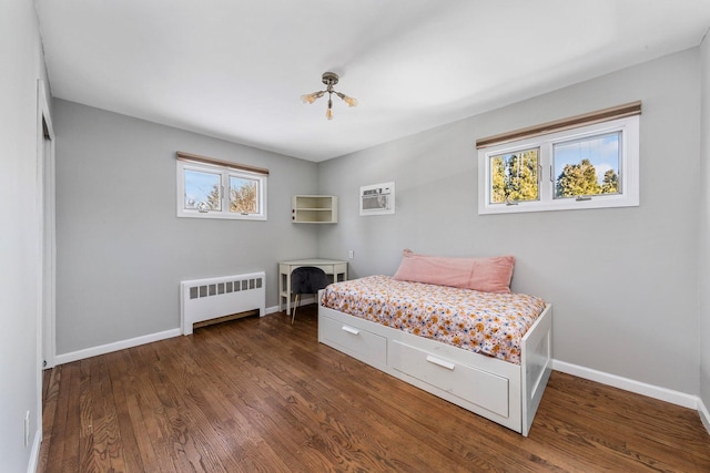 bedroom featuring dark wood-style floors, baseboards, a wall unit AC, and radiator