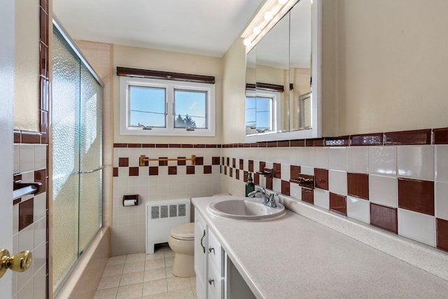 bathroom featuring radiator, toilet, tile patterned floors, vanity, and tile walls