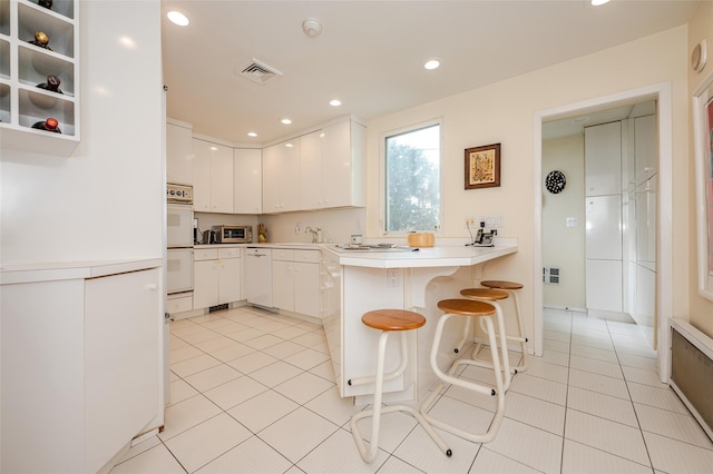 kitchen with kitchen peninsula, a breakfast bar area, white appliances, white cabinets, and sink