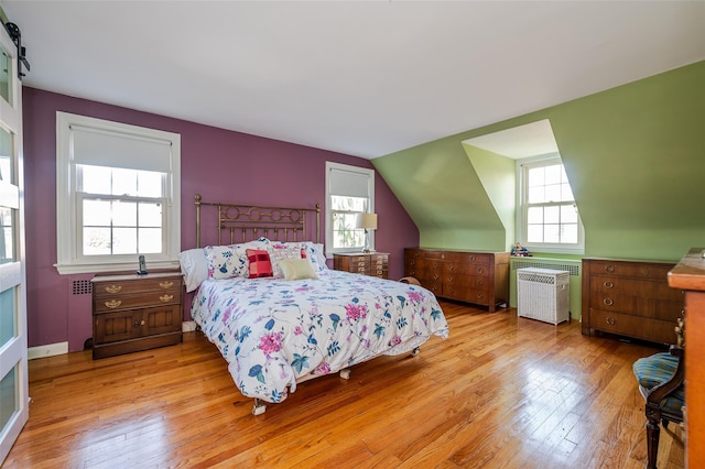 bedroom featuring lofted ceiling, radiator heating unit, and light hardwood / wood-style flooring