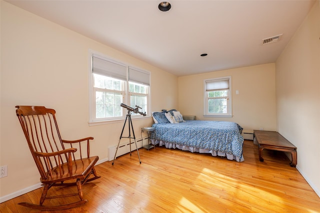 bedroom with a baseboard heating unit, multiple windows, and hardwood / wood-style floors