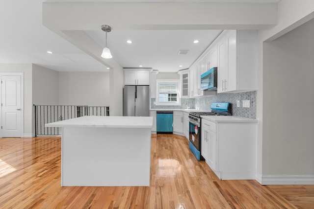 kitchen with white cabinets, appliances with stainless steel finishes, a kitchen island, hanging light fixtures, and light hardwood / wood-style flooring