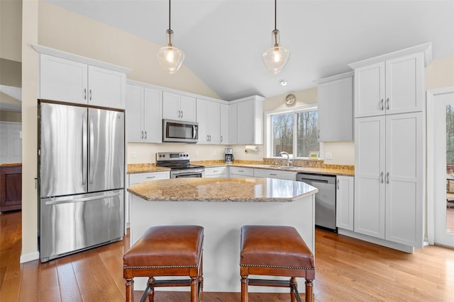 kitchen with vaulted ceiling, pendant lighting, a center island, stainless steel appliances, and white cabinets