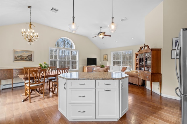 kitchen featuring white cabinetry, hanging light fixtures, stainless steel refrigerator, ceiling fan with notable chandelier, and light stone counters