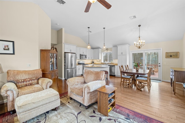 living room with vaulted ceiling, plenty of natural light, ceiling fan with notable chandelier, and light hardwood / wood-style floors