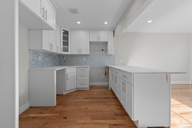 kitchen with kitchen peninsula, backsplash, white cabinets, light hardwood / wood-style flooring, and sink