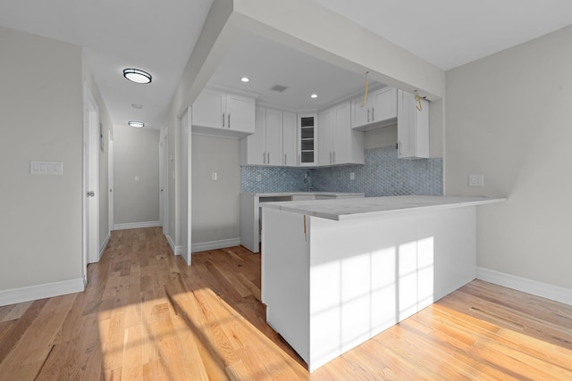 kitchen with tasteful backsplash, kitchen peninsula, white cabinetry, and light hardwood / wood-style flooring