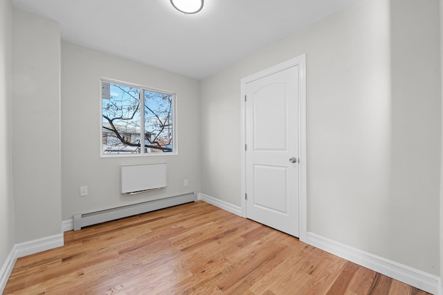 unfurnished room featuring a baseboard heating unit and light wood-type flooring