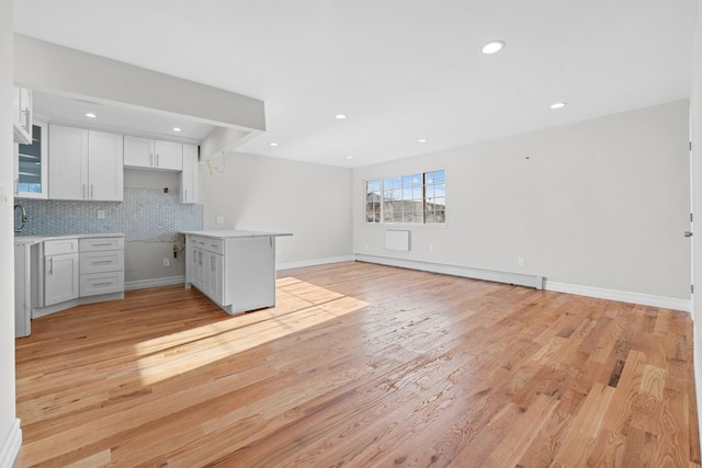 kitchen featuring a baseboard radiator, white cabinets, light hardwood / wood-style flooring, and tasteful backsplash