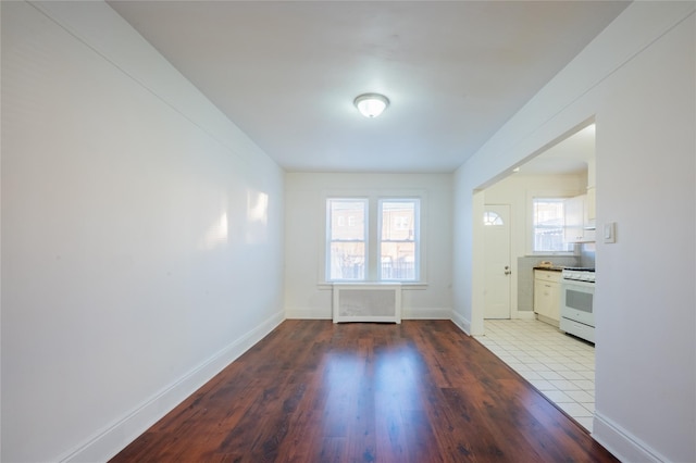 interior space with radiator heating unit, white cabinets, hardwood / wood-style flooring, and gas range gas stove