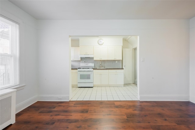 kitchen with hardwood / wood-style floors, white cabinets, radiator, a wealth of natural light, and white gas stove