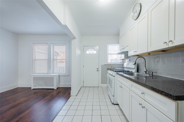 kitchen with white gas range oven, a healthy amount of sunlight, white cabinets, and sink