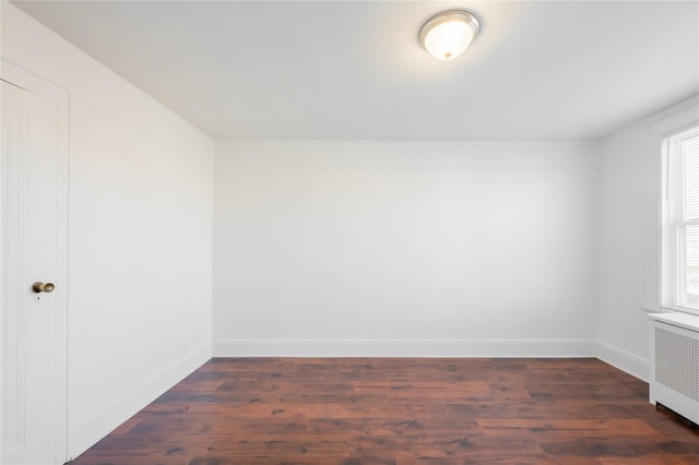 empty room featuring a wealth of natural light, radiator heating unit, and dark hardwood / wood-style flooring