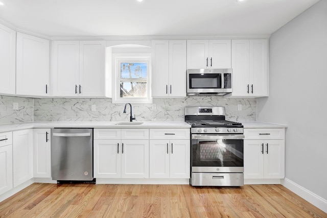 kitchen featuring white cabinetry, stainless steel appliances, decorative backsplash, light hardwood / wood-style flooring, and sink