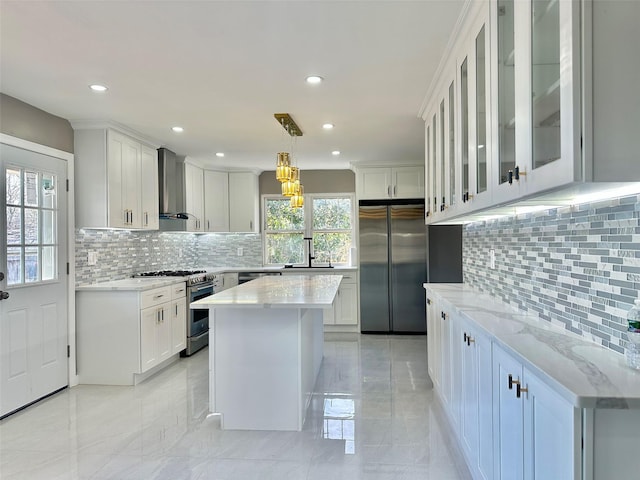 kitchen featuring decorative light fixtures, stainless steel appliances, glass insert cabinets, white cabinets, and wall chimney range hood