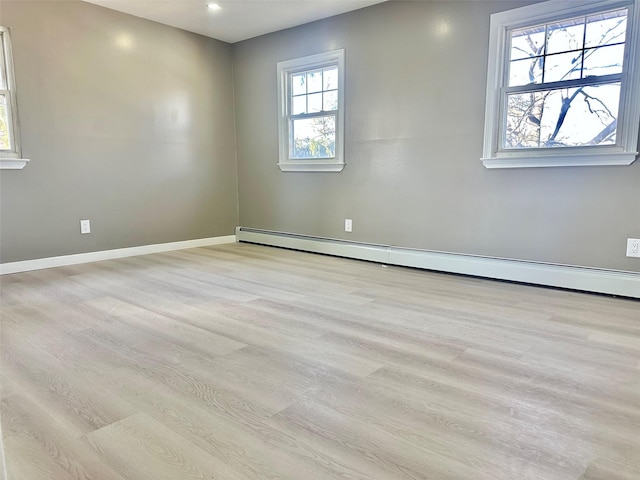 spare room featuring baseboard heating, light wood-type flooring, and baseboards