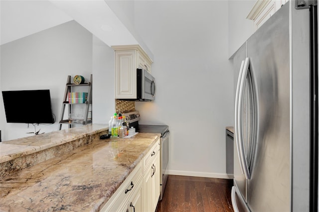 kitchen featuring dark wood-type flooring, stainless steel appliances, backsplash, light stone counters, and cream cabinetry