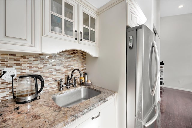 kitchen featuring light stone countertops, white cabinetry, sink, backsplash, and stainless steel fridge