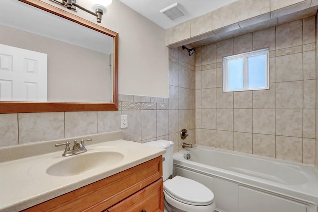 full bathroom featuring tiled shower / bath combo, toilet, vanity, and tile walls