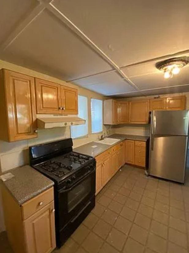 kitchen featuring black gas range, sink, and stainless steel refrigerator