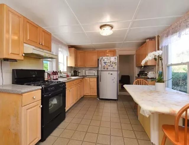 kitchen featuring backsplash, fridge, black gas stove, and light brown cabinets