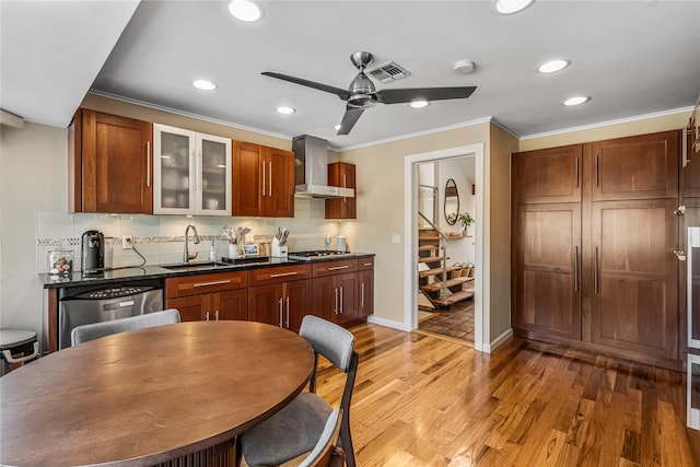 kitchen featuring appliances with stainless steel finishes, wall chimney range hood, tasteful backsplash, sink, and hardwood / wood-style flooring