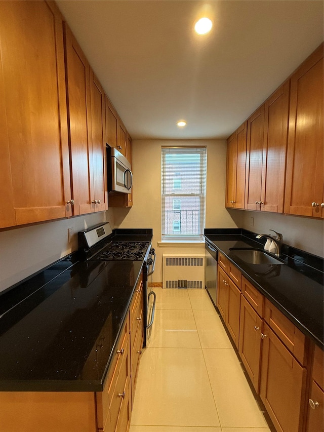 kitchen with appliances with stainless steel finishes, radiator heating unit, dark stone counters, sink, and light tile patterned flooring