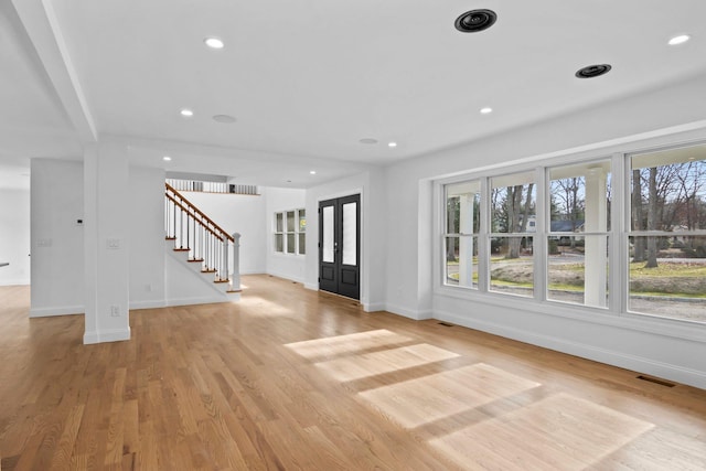 unfurnished living room with light wood-type flooring, a wealth of natural light, and french doors