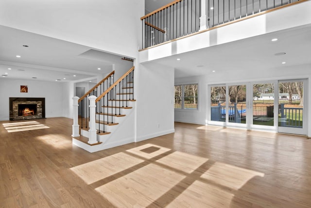 unfurnished living room with a high ceiling, a stone fireplace, and light wood-type flooring