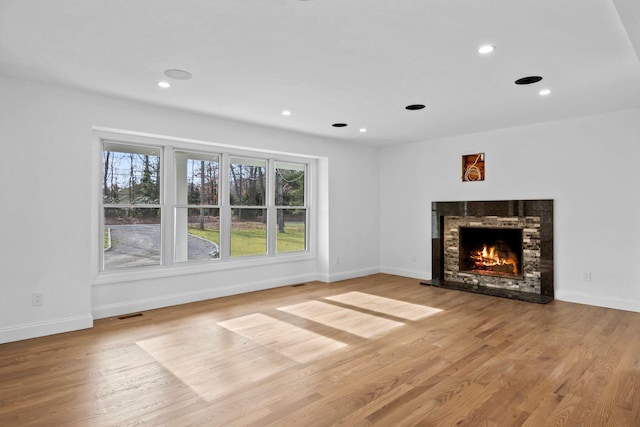 unfurnished living room with light hardwood / wood-style floors and a stone fireplace