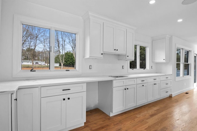 kitchen featuring light wood-type flooring, sink, light stone counters, and white cabinetry