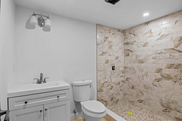 bathroom with toilet, a tile shower, and vanity