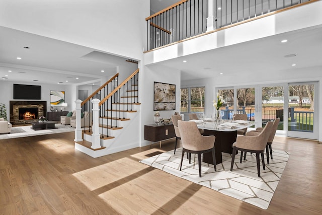 dining area featuring a fireplace, light wood-type flooring, a high ceiling, and a wealth of natural light