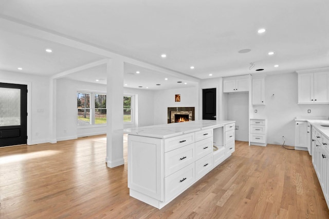 kitchen with a kitchen island, light stone countertops, white cabinets, and light wood-type flooring