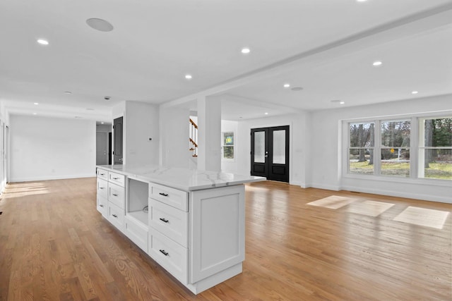 kitchen with white cabinetry, a center island, light stone counters, french doors, and light wood-type flooring
