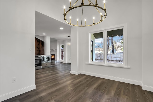 unfurnished dining area featuring a large fireplace, dark hardwood / wood-style flooring, and a notable chandelier